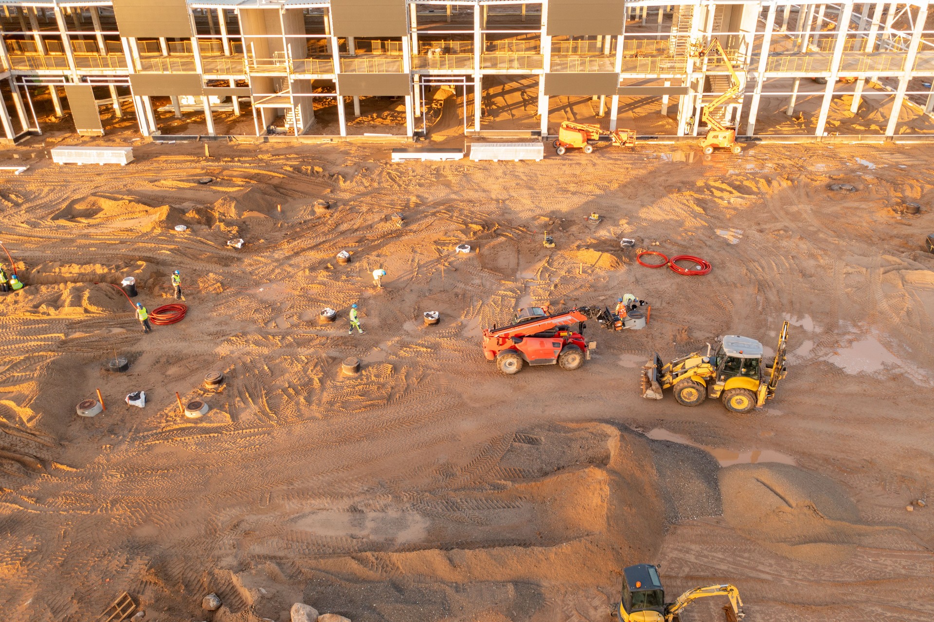 Drone photography of constructions site of large commercial building with construction machinery and construction workers during autumn morning